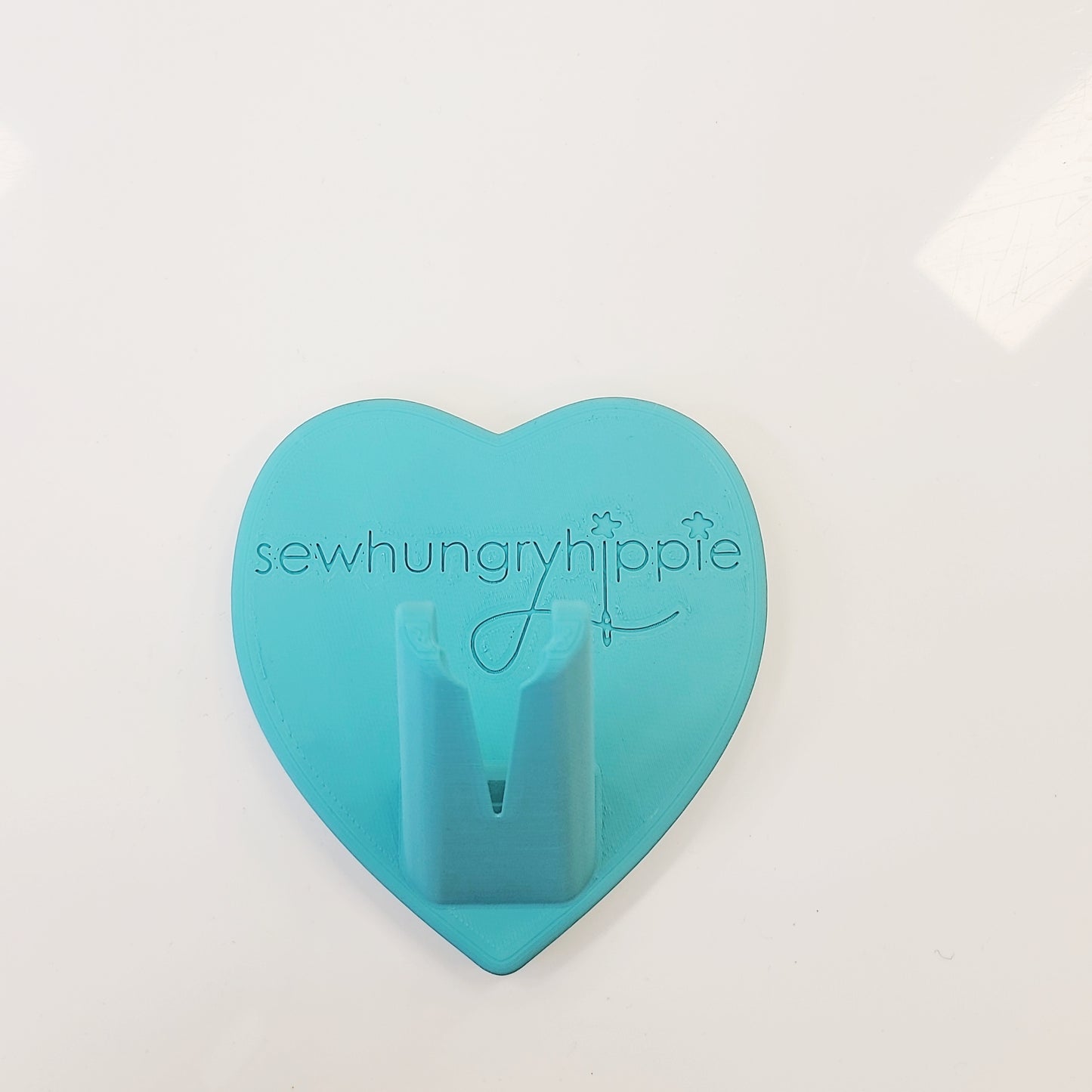 Teal heart-shaped sewing tool holder with logo.