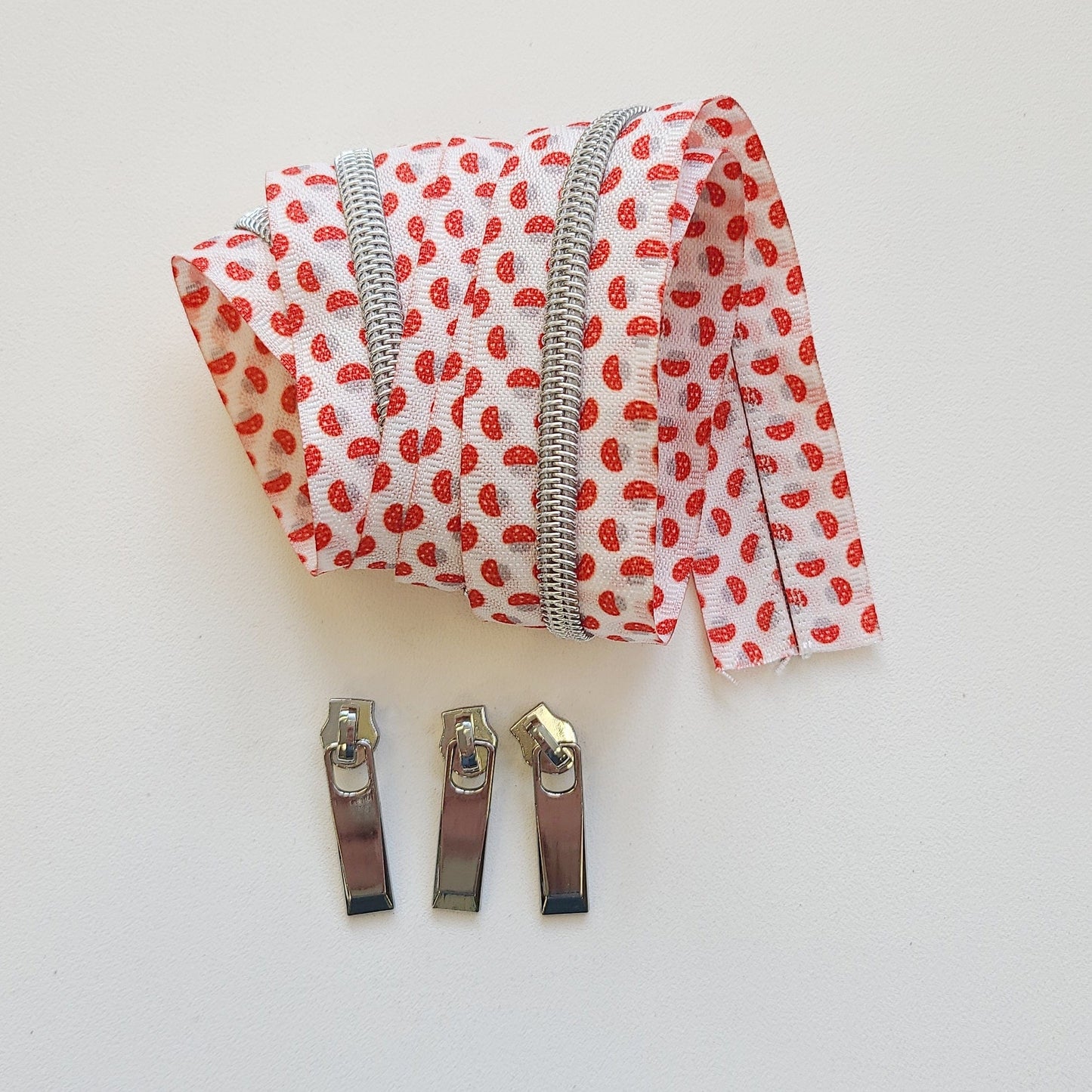 Rolled fabric zipper with red print and three silver zipper pulls.