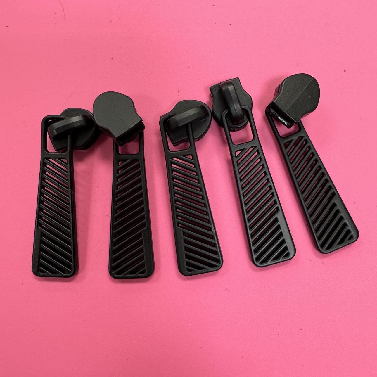 Five black zipper pulls on a pink background.