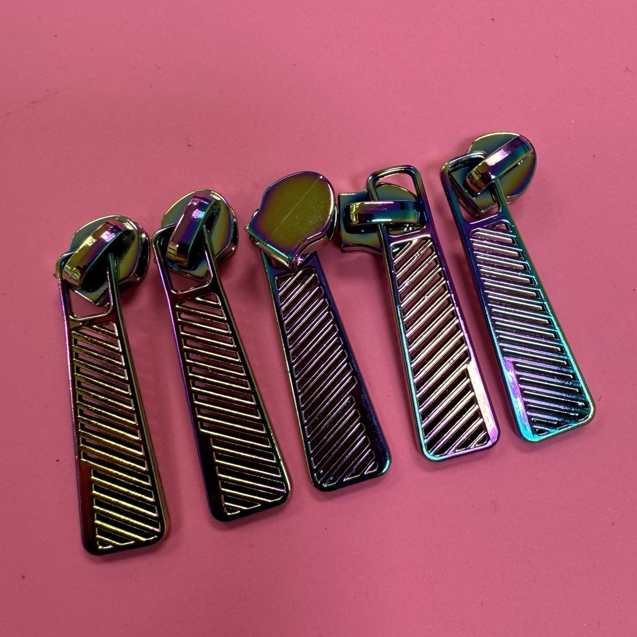 Five iridescent zipper pulls on pink background.