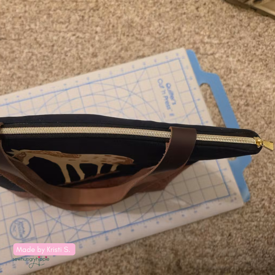 Brown leather pouch with gold zipper on a cutting mat, with 'Made by Krist S' label.