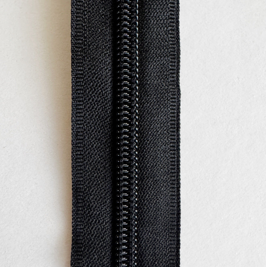 A close-up of a black metal zipper with a black fabric tape, shown vertically against a plain white background.