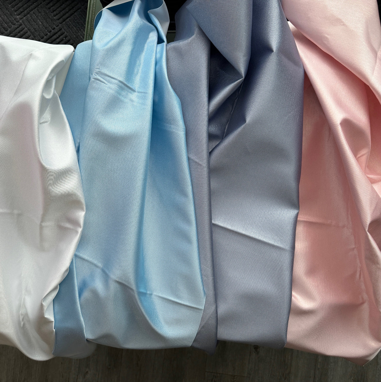 A collection of four different fabric swatches in white, light blue, grey, and light pink displayed side-by-side.