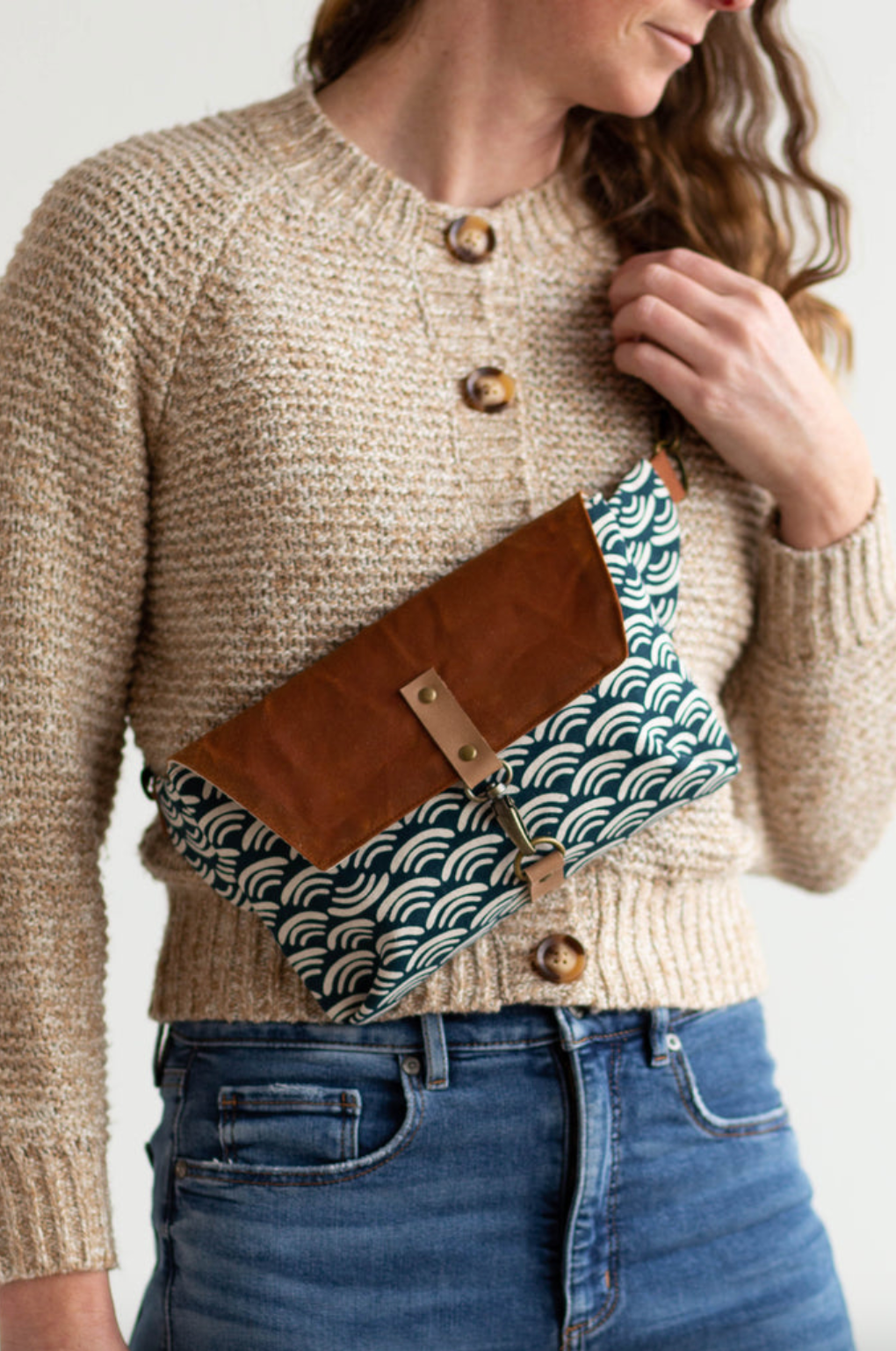 Person wearing a beige sweater with a brown and patterned waist bag.