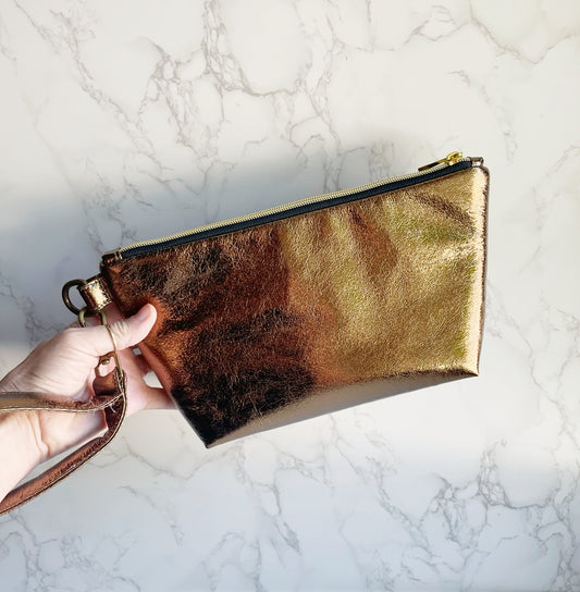 Hand holding a metallic gold clutch with wrist strap.