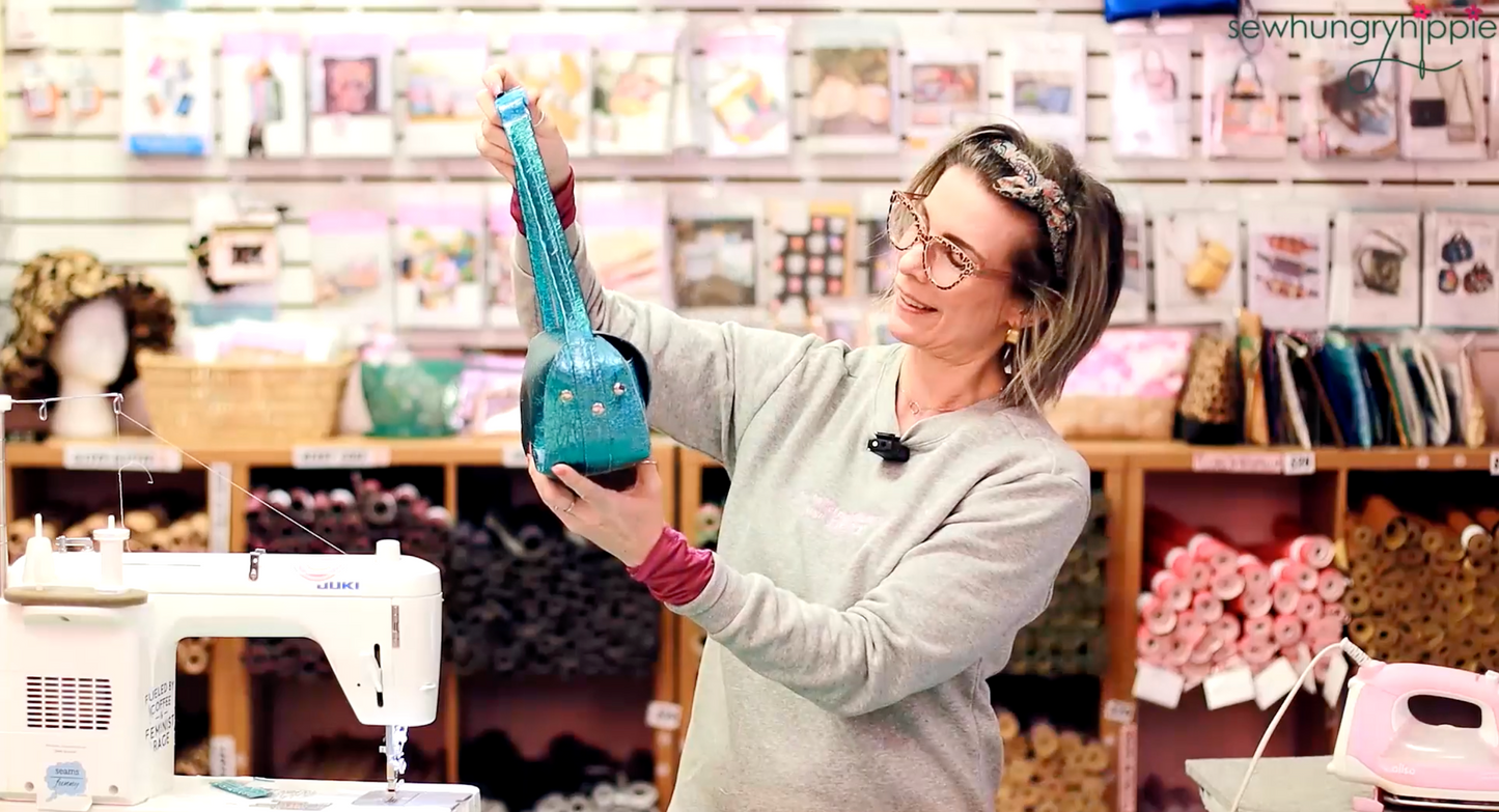 Natalie holding and looking at a handmade blue Jackie Bag in the Sew Hungry Hippie sewing studio