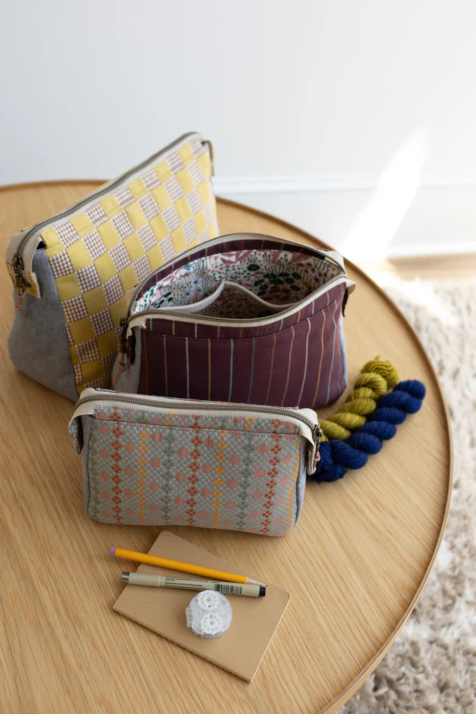 Three patterned pouches on a wooden surface with yarn and stationery items.