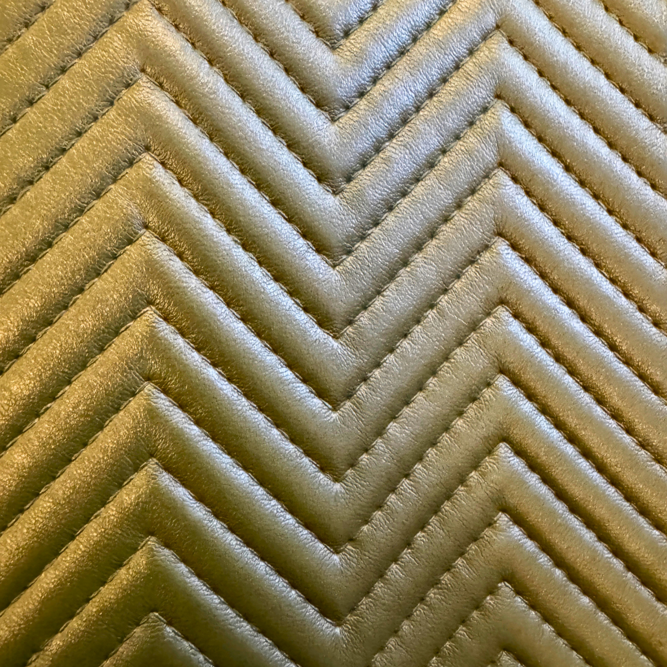 Closed up luxury padded chevron vinyl fabric roll with textured stitched pattern in olive beige tone, photographed for sewing, bag making, and upholstery material listing.