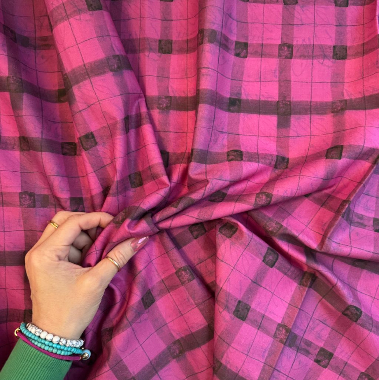 Hand holding a magenta pink and black artistic grid plaid cotton fabric for quilting, apparel, and sewing projects.