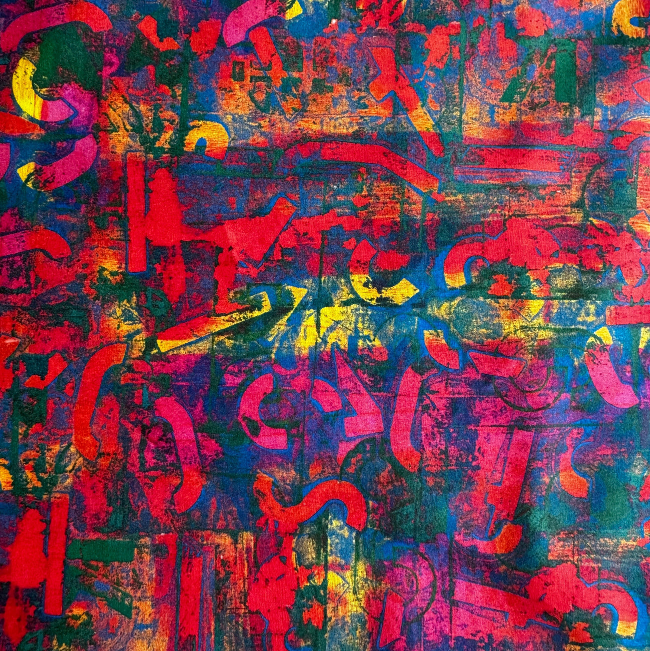 Close-up flat lay of an abstract print fabric with overlapping red, yellow, and blue geometric shapes on a textured, multi-colored background.