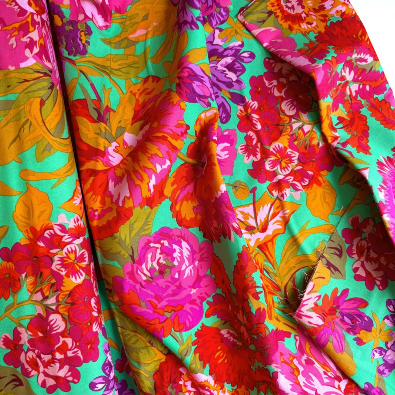 Kaffe Fassett Collective February 2026 Collection. Vibrant, draped floral fabric featuring large pink, orange, and purple flowers on a bright mint green background.