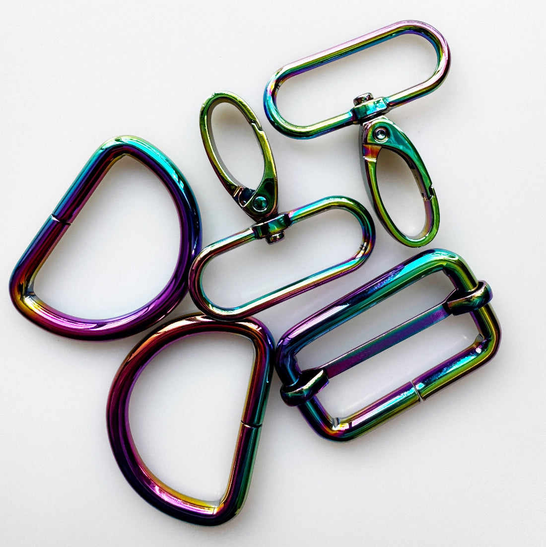 Five metallic hardware pieces iridescent rainbow finish, arranged on a plain white background.
