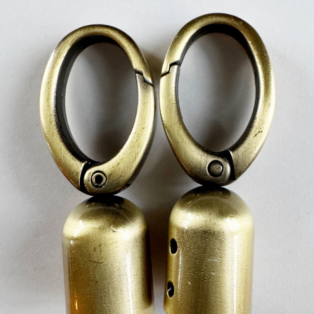 Pair of brass tassel caps on a reflective surface with a light gray background