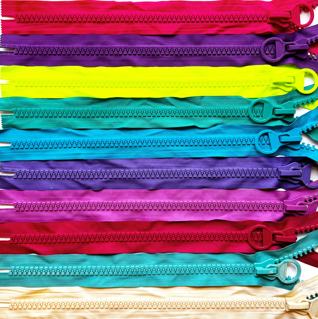 A stack of colorful fabric zipper tapes laid flat, showing multiple vibrant color options including red, purple, neon yellow, teal, blue, pink, magenta, and cream.