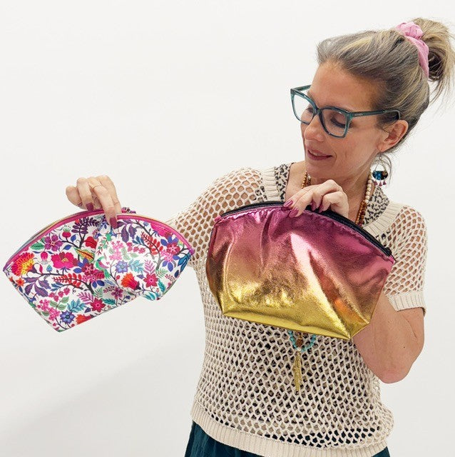 Woman holding a floral makeup bag and a pink metallic pouch against a white background