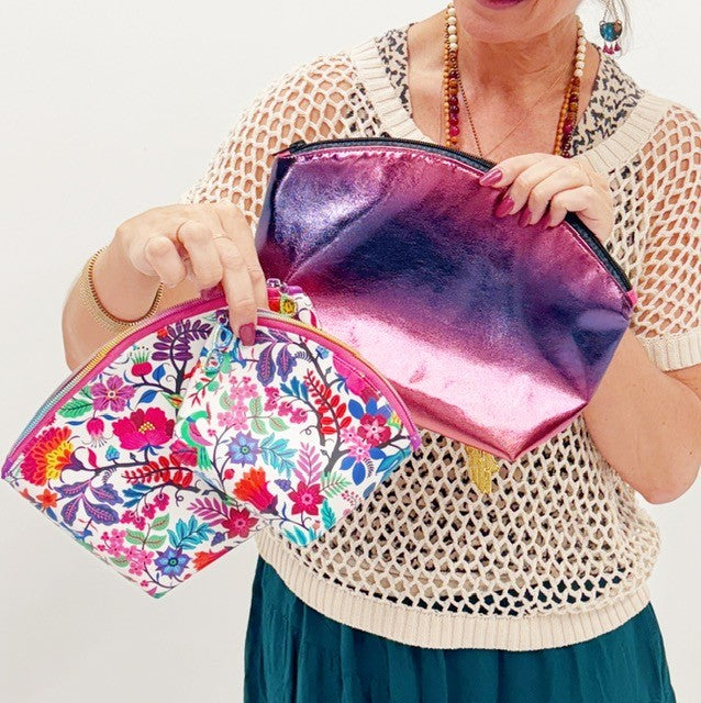 Person holding two clutch bags, one floral and one metallic pink, against a white background