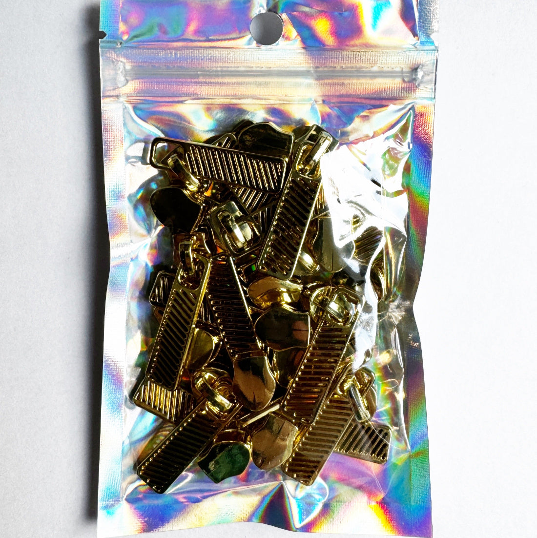 A clear holographic zip pouch containing multiple gold-toned metal hair claw clips, photographed against a plain white background.