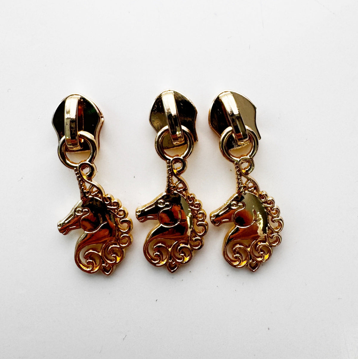 Three gold-colored metal Unicorn Zipper Pulls designed for #5 nylon zipper tape