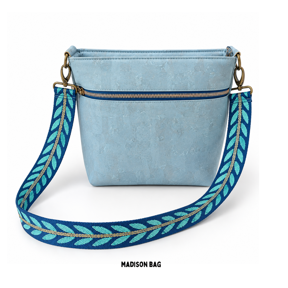 Image of a powder blue cork crossbody bag featuring an exterior zipper pocket and a wide blue and teal strap with a leaf pattern.