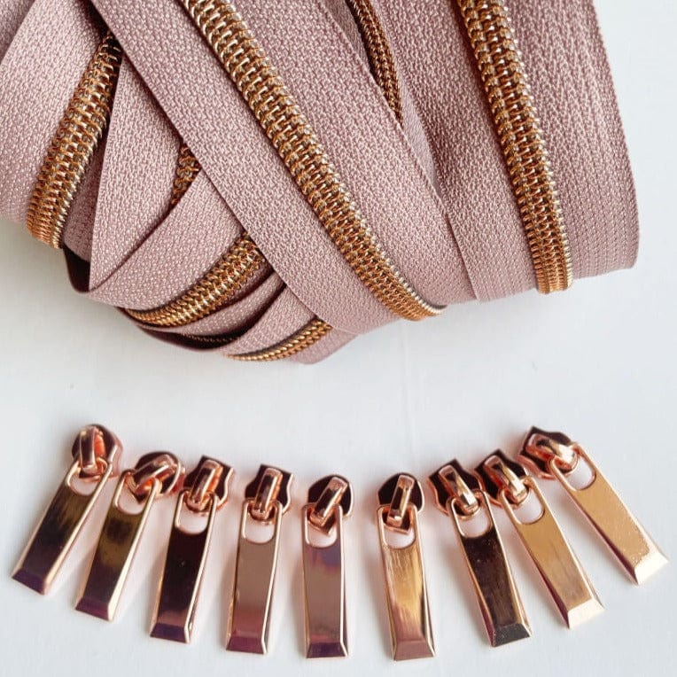 Rose gold zipper pulls and its matching tape, arranged in a parabolic shape, zoomed in for detail.