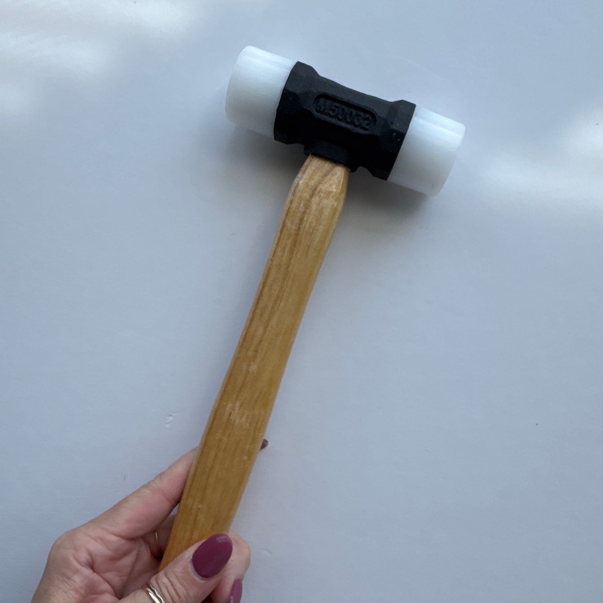 Hand holding a mallet with a wooden handle and white head on a light gray background