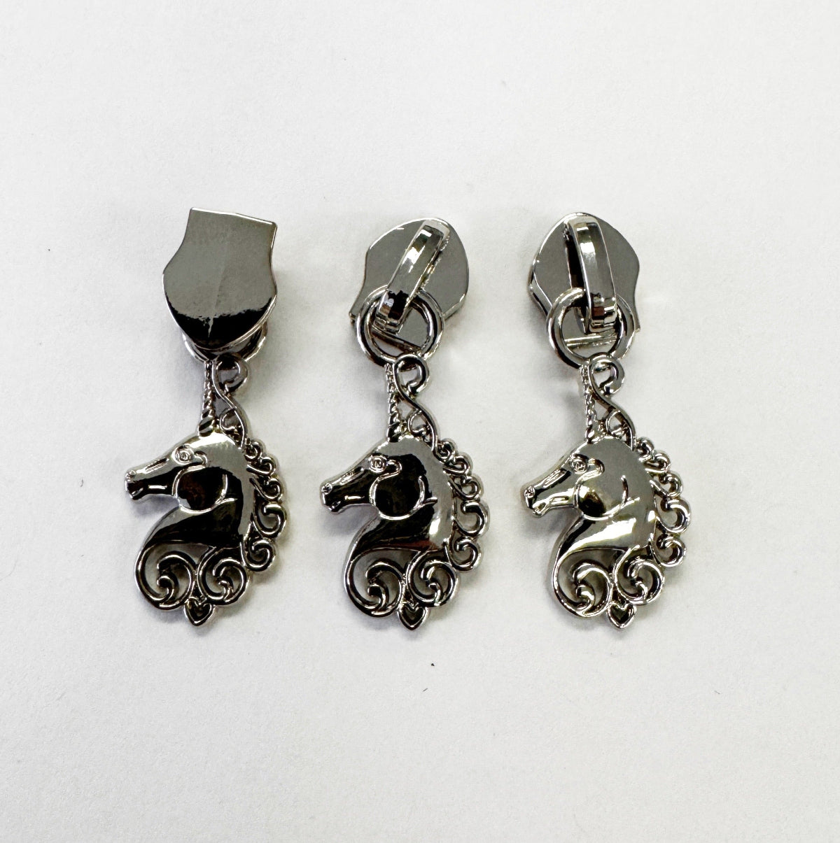 Three silver-toned unicorn-shaped zipper pulls with shield-shaped posts, arranged side by side on a plain white background.