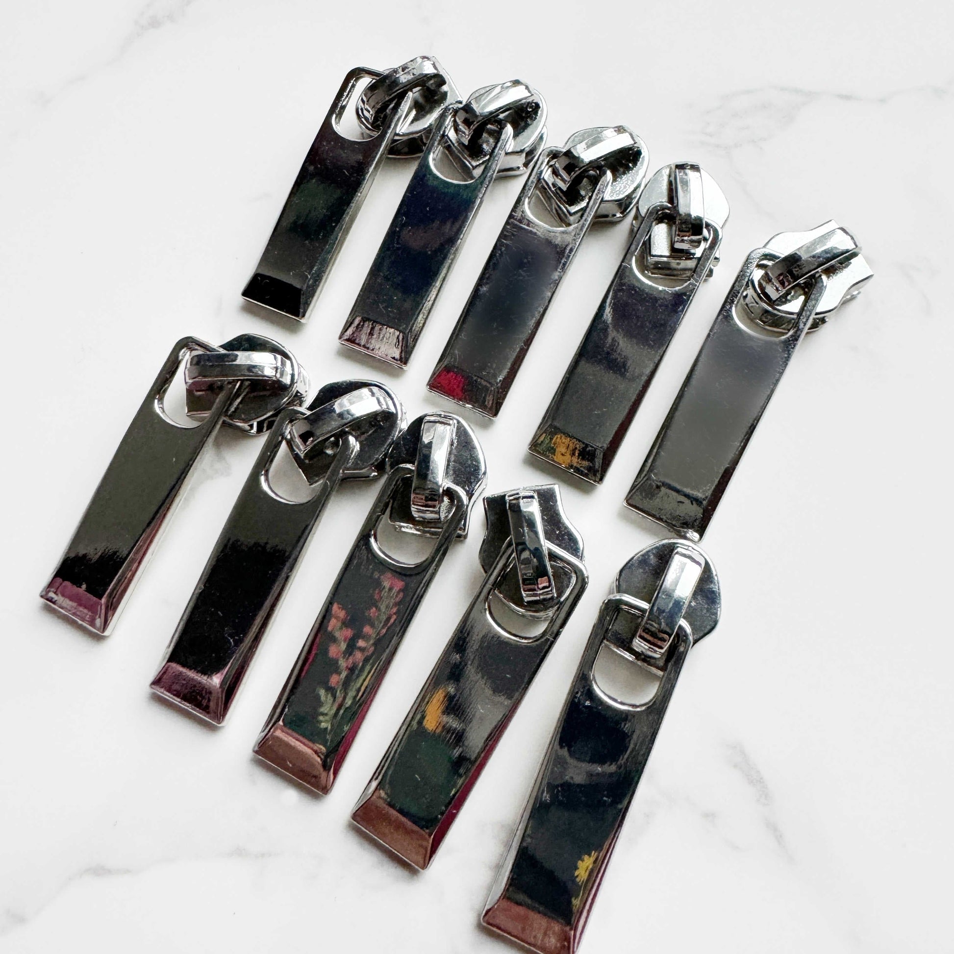 Ten silver zipper pulls arranged in two rows of five.