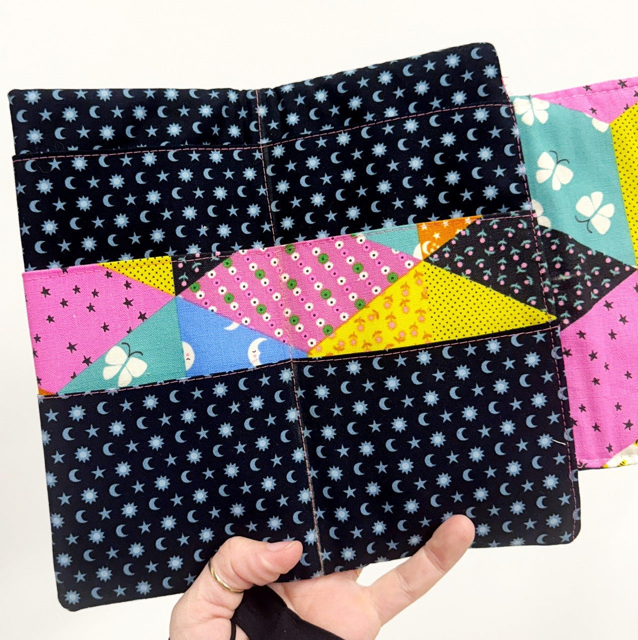 Handmade patchwork pouch held by a hand with various patterns including stars, moons, and geometric shapes.
