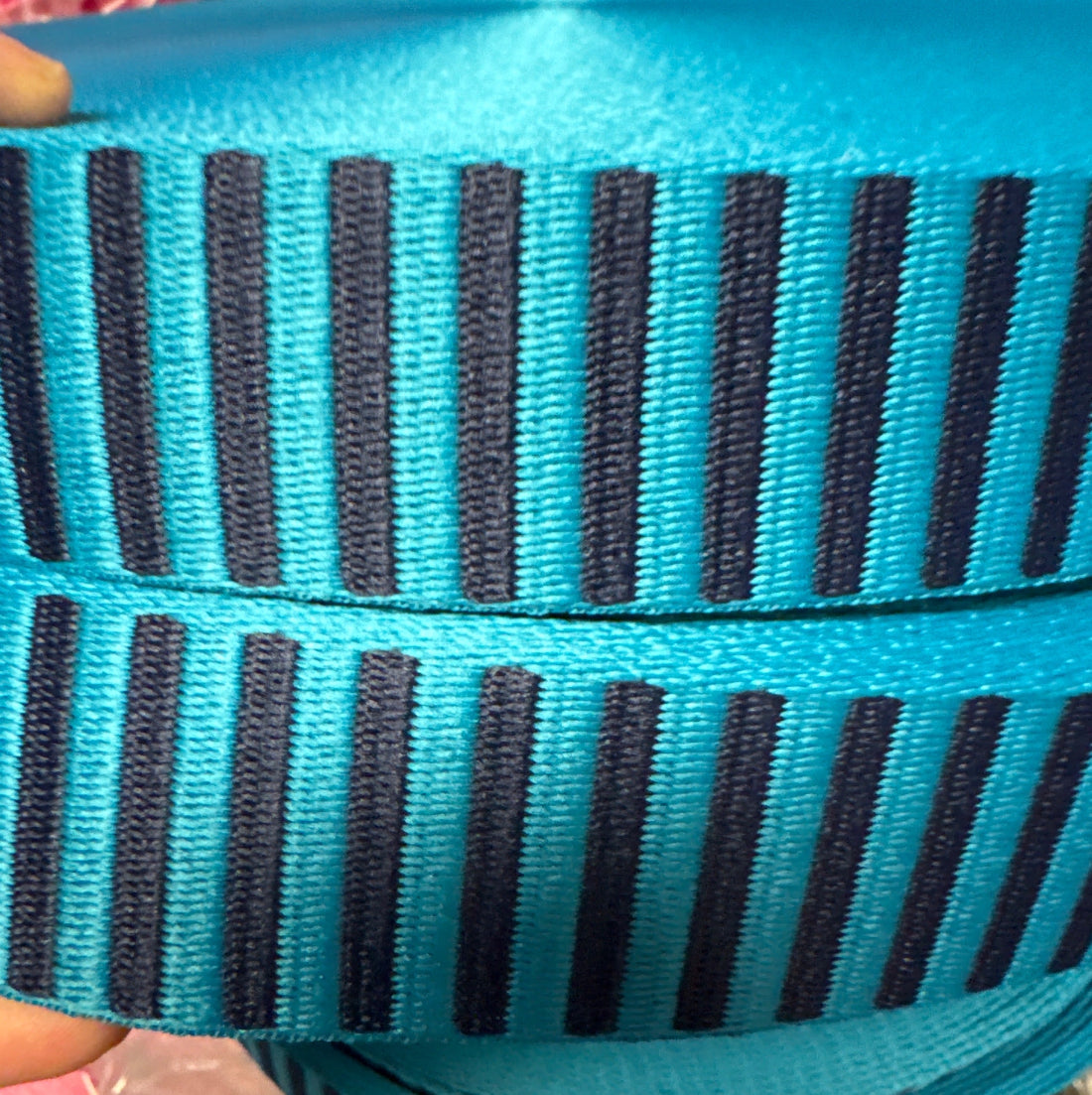 A close-up of a woven ribbon or trim with alternating vertical stripes in bright turquoise blue and dark navy blue.