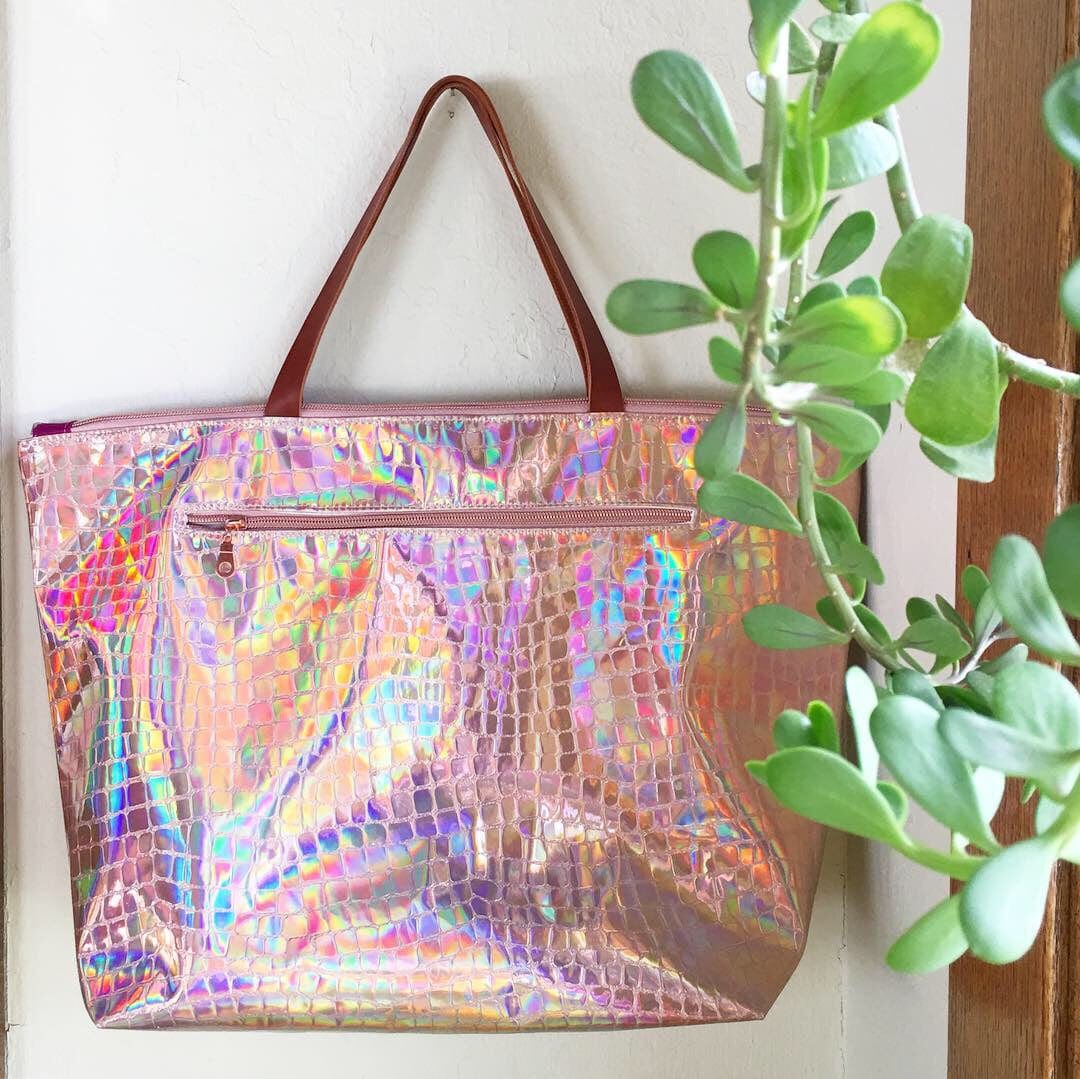 Pink holographic tote bag with brown handles and succulent plant.