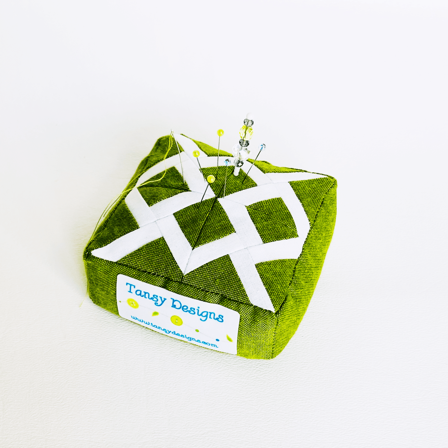 Green and white patterned pin cushion with pins.