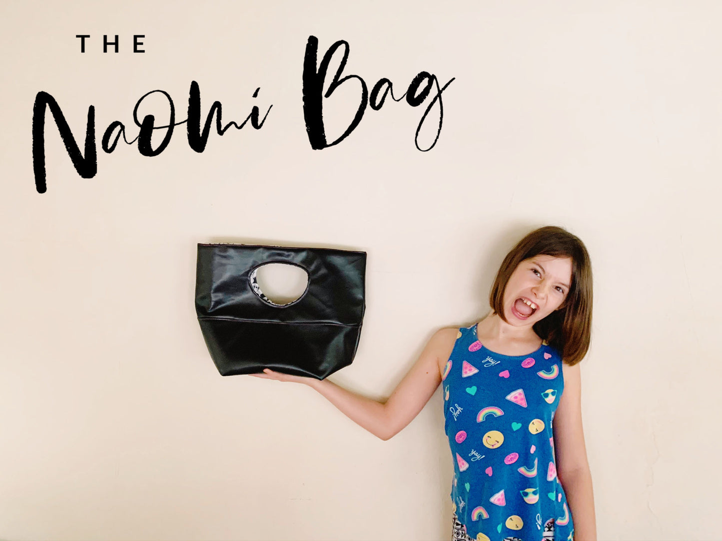 Girl holding a black bag with a hole, text reads The Naomi Bag.
