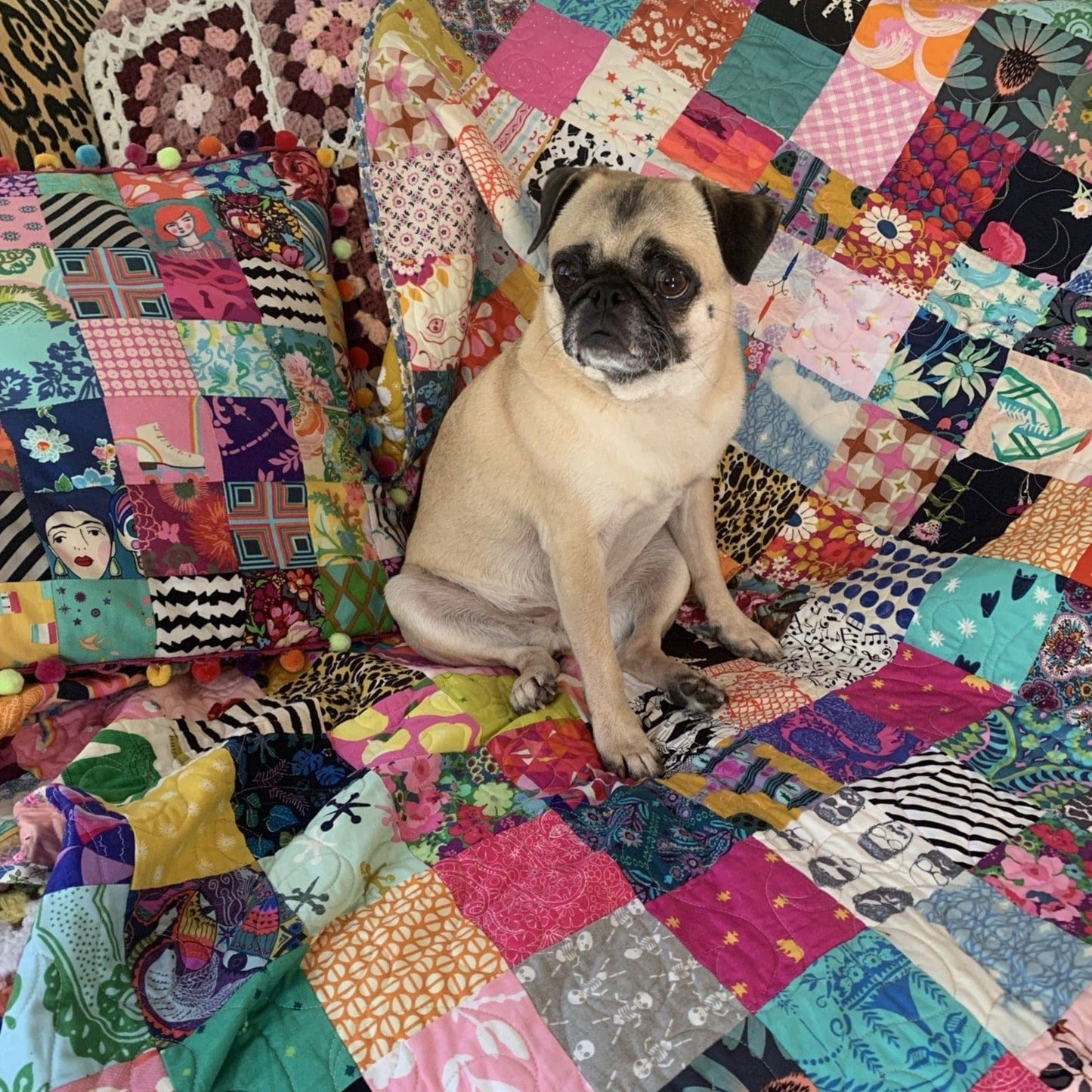 Pug dog sitting on a colorful patchwork quilt.