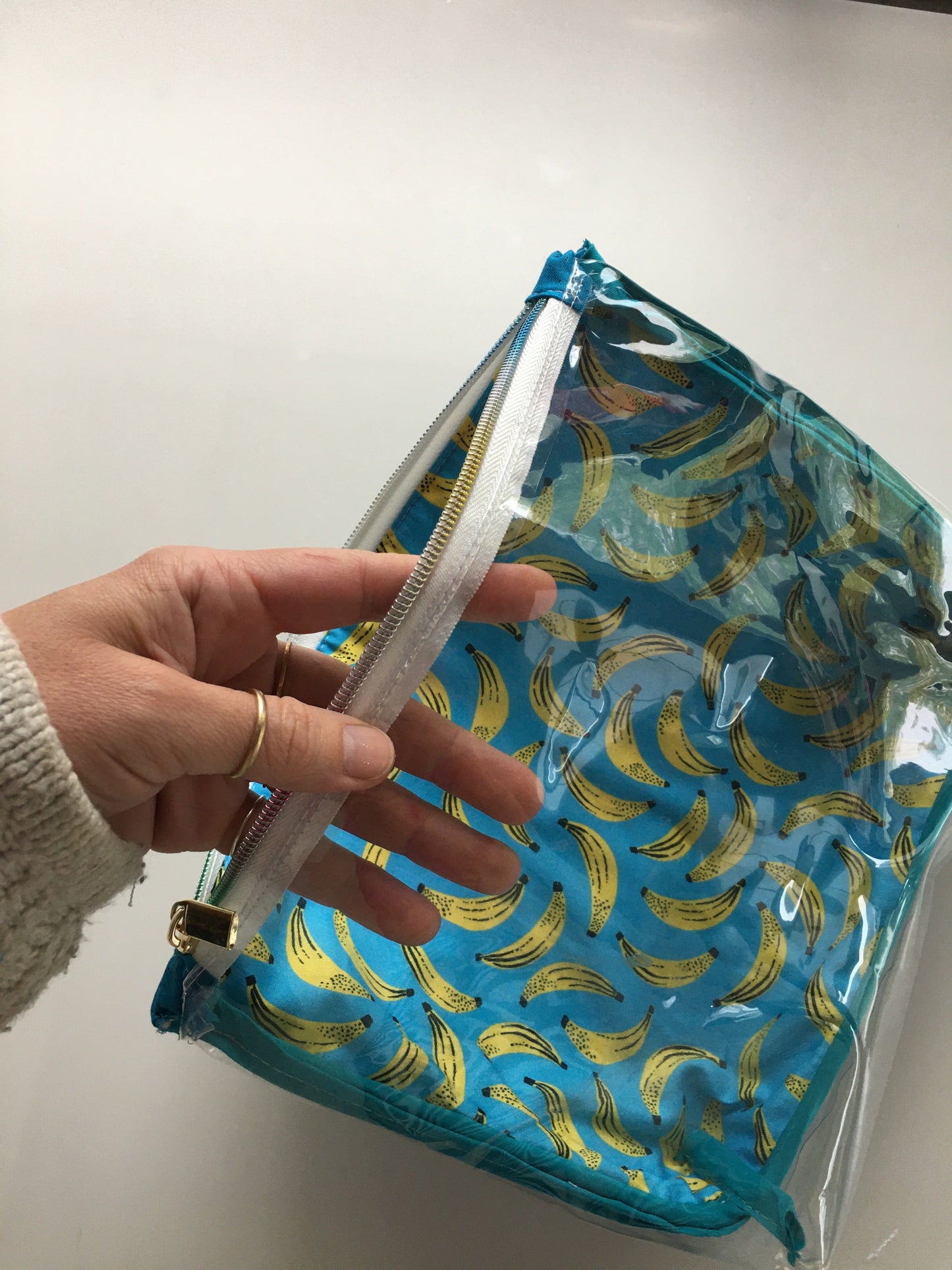 Hand holding a clear cosmetic bag with banana print.