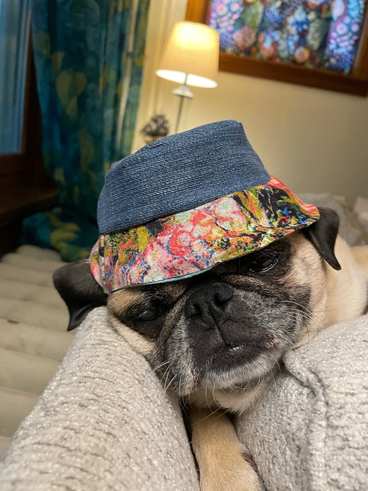 Pug dog wearing a denim and floral hat, sleeping.