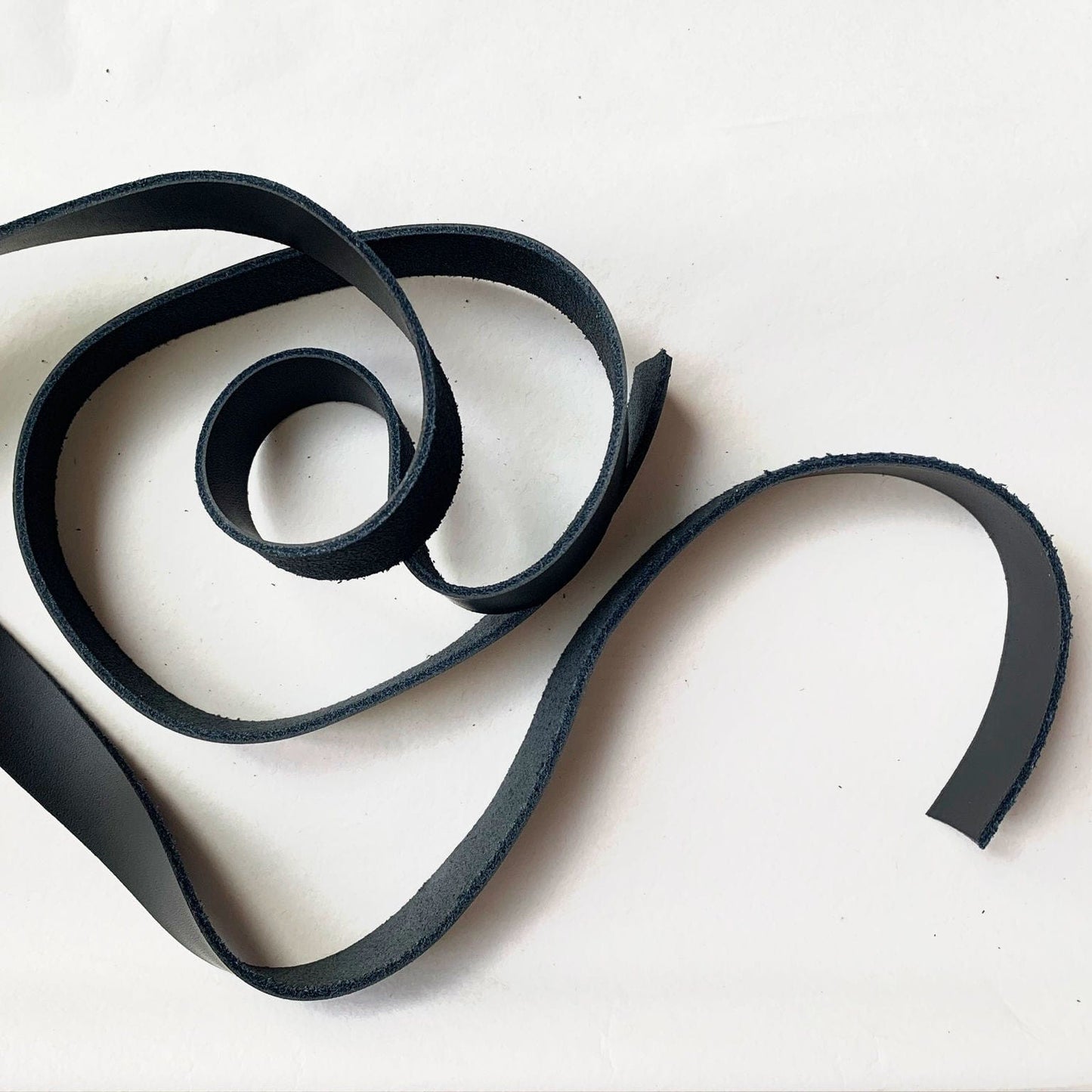 Black leather strap coiled on white surface