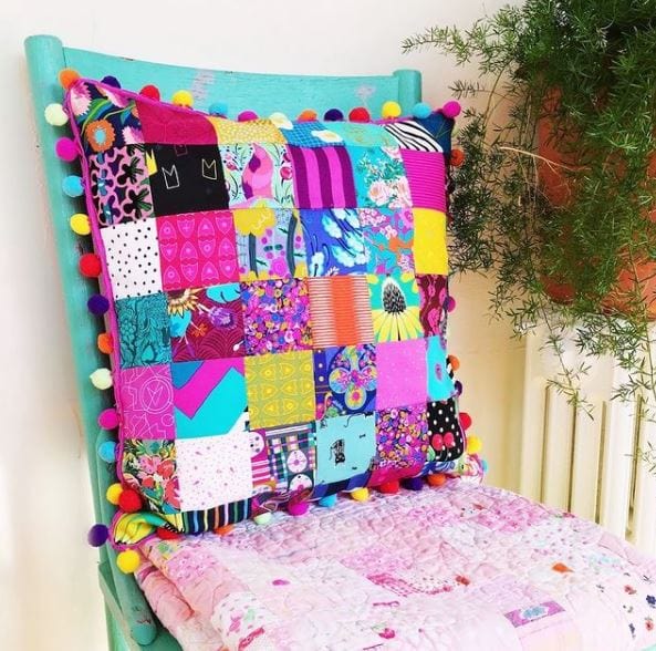 Patchwork pillow with colorful pom-poms on a chair