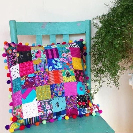 Patchwork pillow with pom-pom trim on turquoise chair