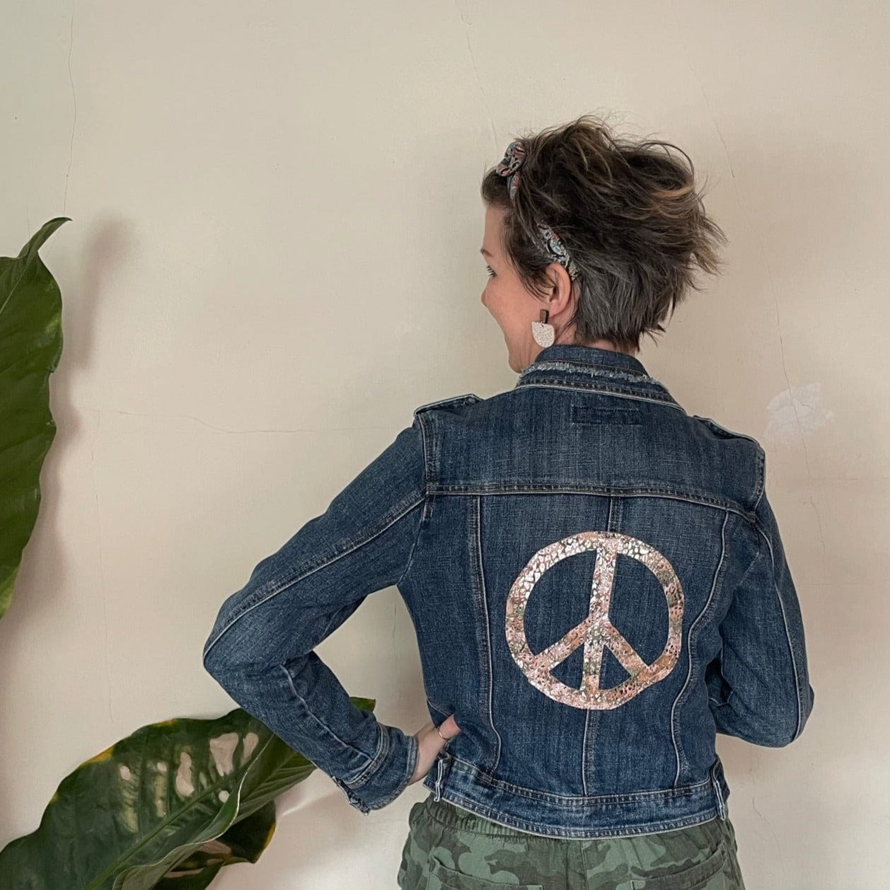Woman wearing denim jacket with peace sign.
