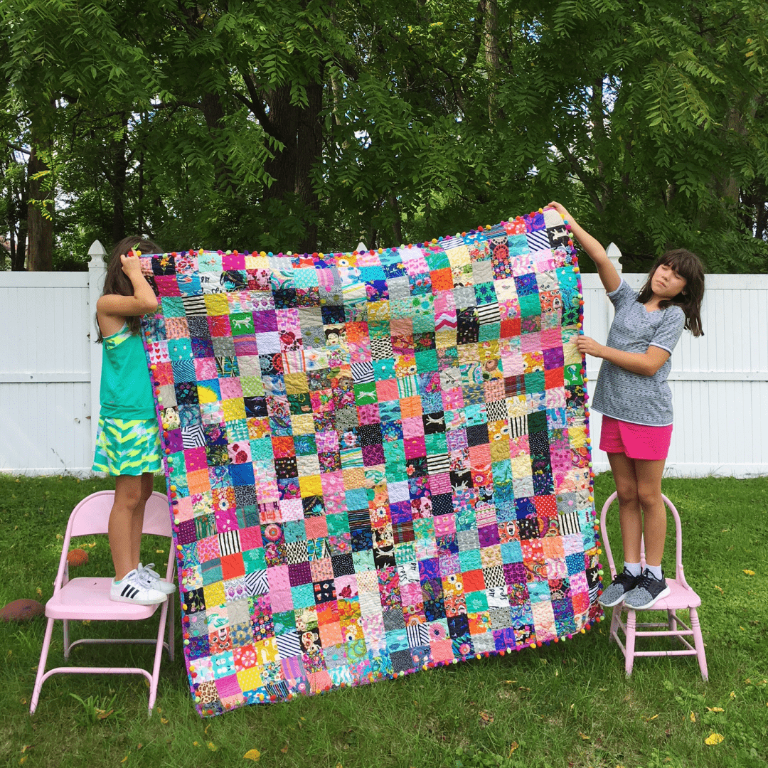 Two girls holding colorful patchwork quilt