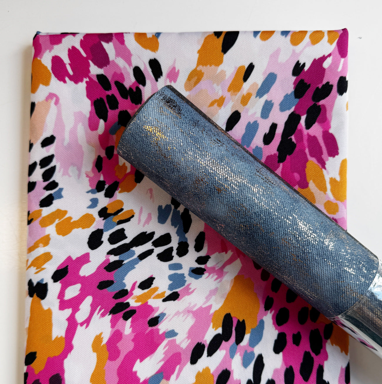 Abstract magenta and mustard yellow painterly patterned fabric coordinates with a textured slate blue gold metallic faux leather roll for sewing and bag making.