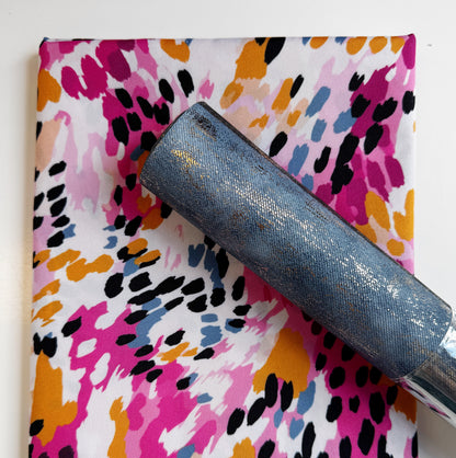 Abstract magenta and mustard yellow painterly patterned fabric coordinates with a textured slate blue gold metallic faux leather roll for sewing and bag making.