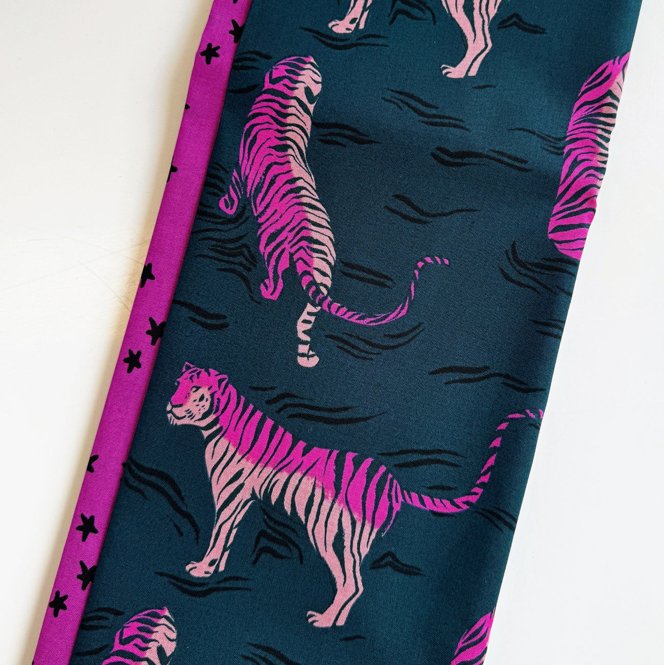 Dark teal canvas fabric with a neon pink and black tiger illustration print paired with a coordinating magenta pink star print cotton fabric for bag making and quilting.