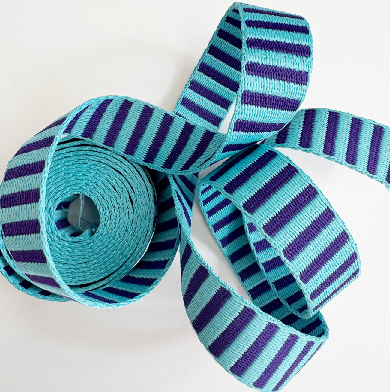 Coiled 1-inch wide woven striped webbing in teal blue and deep purple for bag straps.