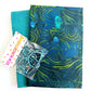 A craft bundle containing two yards of fabric, including a solid teal textile and a patterned blue and green abstract print, paired with a pack of matching metallic blue hardware clips from Sew Hungry Hippie.