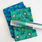 2-yard craft bundle featuring two folded cotton fabrics with teal and blue floral and ginkgo leaf prints, topped with a roll of green iridescent faux leather vinyl
