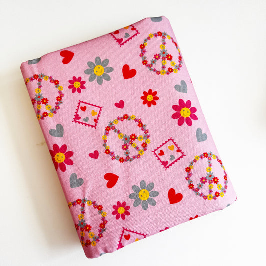 Pink fabric with peace signs, flowers, and hearts on a white background