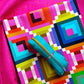 Fuschia pink speckled fabric in the background and a yard folded of geometric Happy Place collection by Annabel Wrigley for Windham Fabrics and coordinating turquoise zipper tape in rainbow teeth.