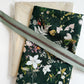 Dark forest green canvas fabric featuring a woodland wildflower botanical pattern, paired with a cream linen base fabric and a sage green nylon coil zipper tape for custom pouch and bag making.