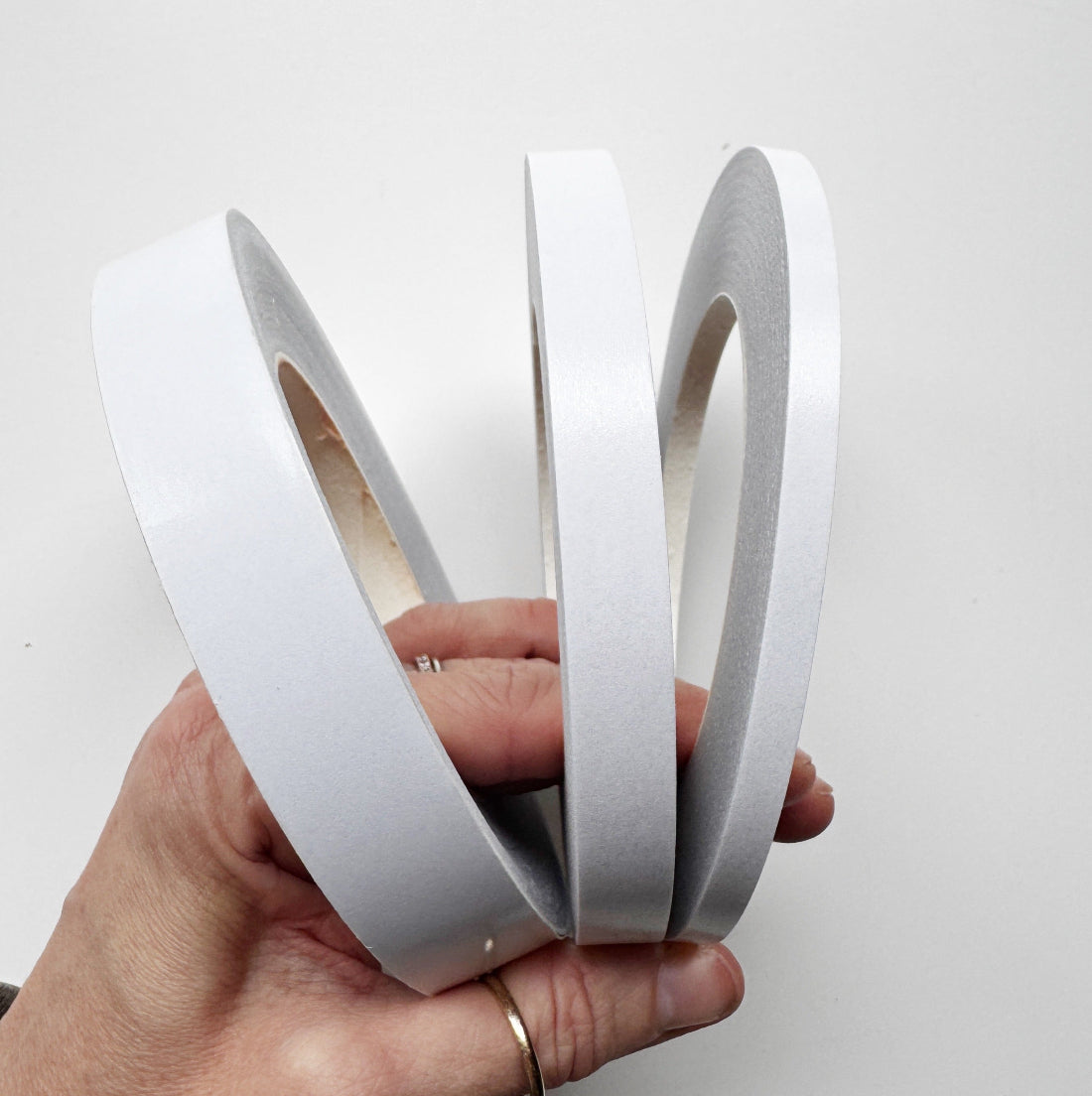 Three rolls of white adhesive tape held together by a person's hand against a plain white background.